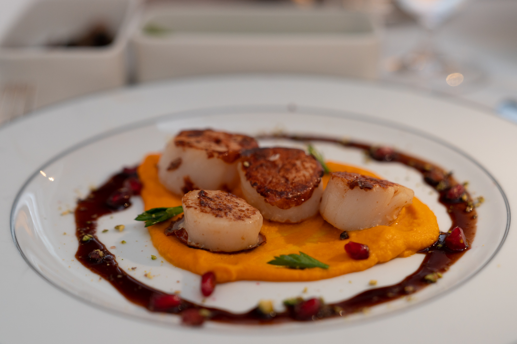 Pan-seared scallops on pumpkin purée, with pomegranate and orange sauce, and pistachios.
