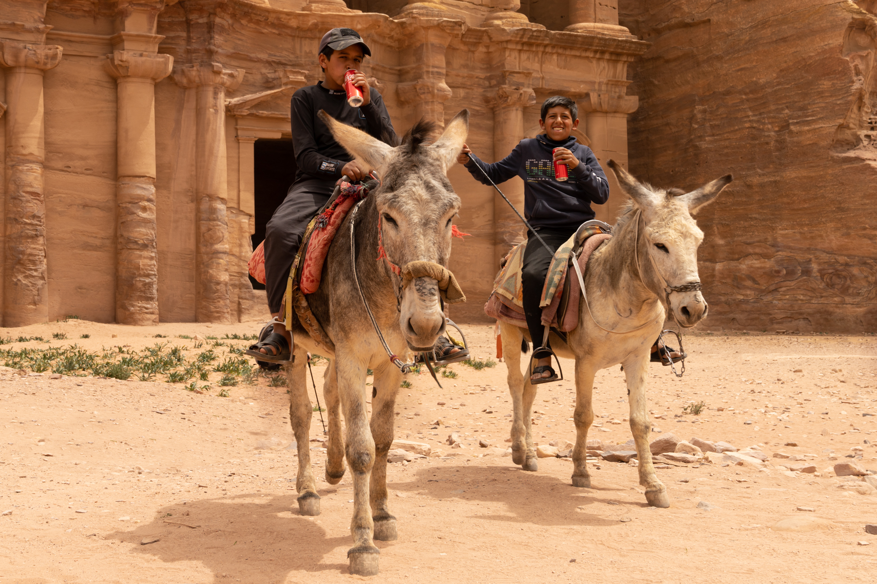 Two boys on donkeys, enjoying cans of Coke!