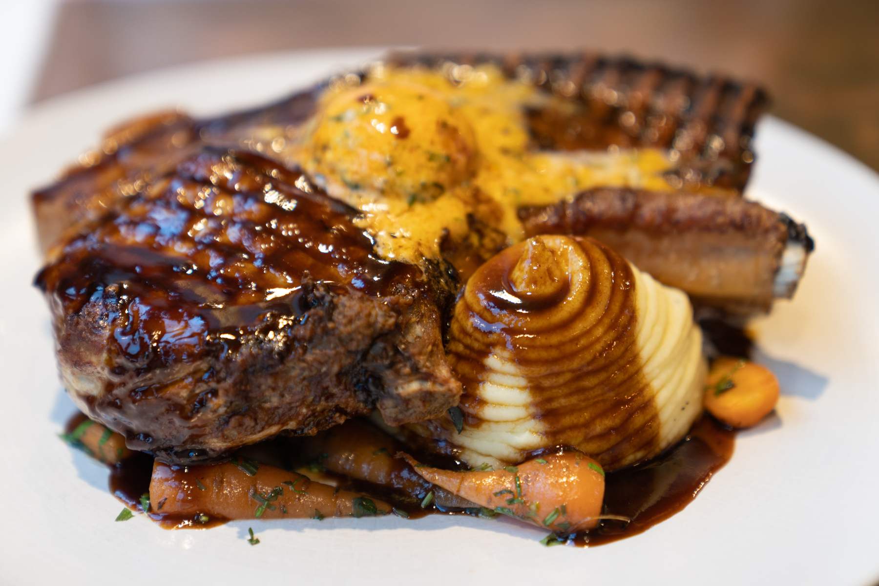 10 oz Rare Breed pork chop with Marmite-buttered Hispi cabbage, Visy Chantenay carrots, mashed potato, Café de Paris butter, red wine jus, and apple sauce.